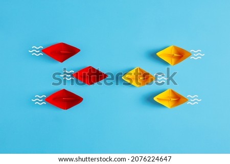 Confrontation, competition, opposition or business challenge concept. Red and yellow paper boat fleet encounter on blue background.
