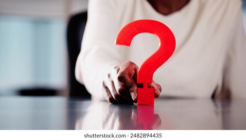 Confused African American Businesswoman Holding Red Question Mark Sign in Corporate Office Desk Asking for Answers