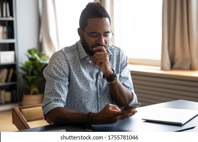 Confused African guy holding smart phone feels concerned thinking over received message. Mobile phone everyday usage, unpleasant news, waiting for important call, low signal device problems concept