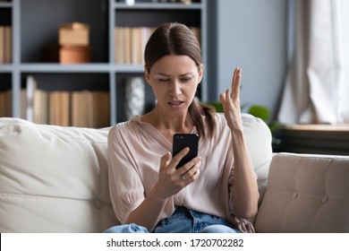Confused angry woman having problem with phone, sitting on couch at home, unhappy young female looking at screen, dissatisfied by discharged or broken smartphone, reading bad news in message