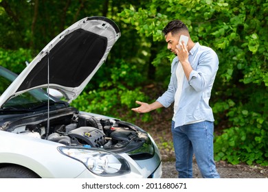 Confused Arab Guy Driver Looking Under Car Hood, Calling Auto Service, Upset Middle-eastern Young Man Got Stuck At Highway, Having Phone Conversation With Friends, Asking For Help, Side View