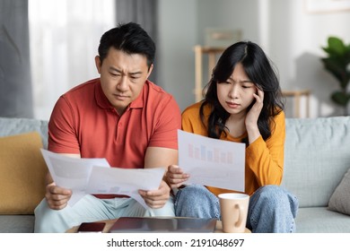 Confused Asian Couple Checking Bills, Sitting On Couch, Reading Documents, Unhappy Chinese Man And Woman Holding Papers, Counting Monthly Spendings, Copy Space. Family Budget Concept