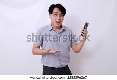 Confused asian man holding a cell phone while showing asking gesture. Isolated on white