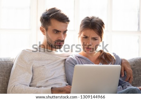 Confused baffled wife and shocked frustrated husband reading online news looking at stuck laptop, bewildered young couple in disbelief perplexed by computer problem email or system failure message