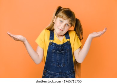 Confused Caucasian Girl Child Shrug As Sign Of Doubt Making Choice. Portrait Of Frustrated Small Kid Looking At Camera Hold Palms Up, Isolated Over Orange Studio Background. People Emotion Concept