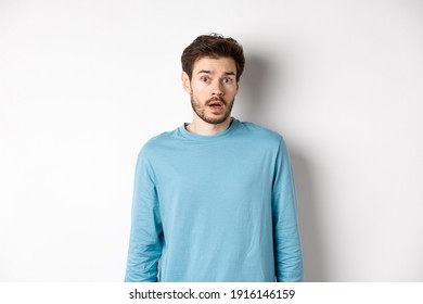 Confused caucasian guy drop jaw and stare startled at camera, standing over white background