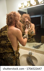 Confused Caveman With Overgrown Hair And Beard Holding A Razor In Front Of The Mirror At The Bathroom Sink