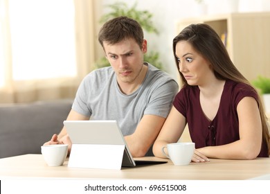 Confused Couple Receiving On Line News Sitting In A Desk At Home