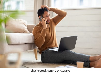 Confused Discontented Arabic Guy Talking On Cell Phone Using Pc Having Problem With Computer Or Internet Connection At Home. Displeased Male Customer Calling To Hotline Service And Complaining