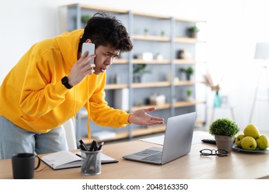 Confused Discontented Asian Man Talking On Phone Using Laptop Having Problem With Computer Or Internet Connection At Home. Displeased Male Customer Calling To Hotline Service And Complaining