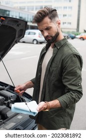 Confused Driver Checking Oil Of Motor Near Car Outdoors