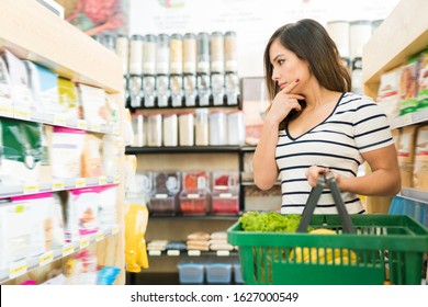 Confused female customer choosing food products on shelf in supermarket