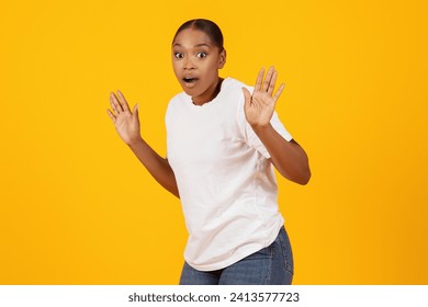 Confused frightened African American lady got caught posing with raised hands looking at camera with scared expression, standing over yellow studio background. It's not me concept
