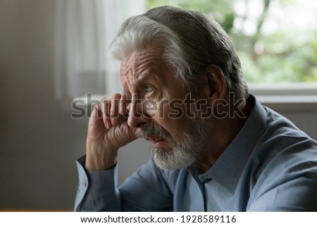 Confused frustrated old 70s aged man rubs face and eye, looks away with unhappy face. Mature elder pensioner suffers from memory loss, cataract, feels stress, lonely, despair. OAP going through grief