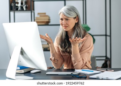 Confused gray-haired mature lady, business woman manager or consultant, looking at the computer in confusion, received an incomprehensible message, or strange news - Powered by Shutterstock