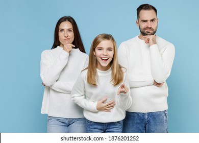 Confused Laughing Young Parents Mom Dad With Child Kid Daughter Teen Girl In White Sweaters Pointing Index Finger On Camera Isolated On Blue Background Studio Portrait. Family Day Parenthood Concept