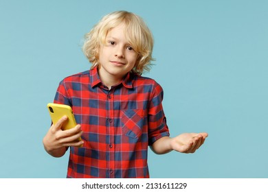 Confused Little Curly Kid Boy 10s In Red Checkered Shirt Using Mobile Cell Phone Typing Sms Message Spreading Hands Isolated On Blue Background Children Studio Portrait. Childhood Lifestyle Concept