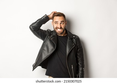 Confused Macho Guy In Black Leather Jacket Looking Awkward And Unsure, Scratching Head Puzzled And Stare Left, White Background