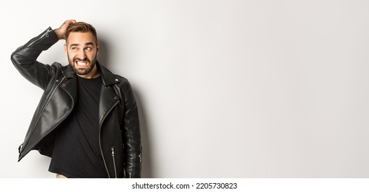 Confused Macho Guy In Black Leather Jacket Looking Awkward And Unsure, Scratching Head Puzzled And Stare Left, White Background
