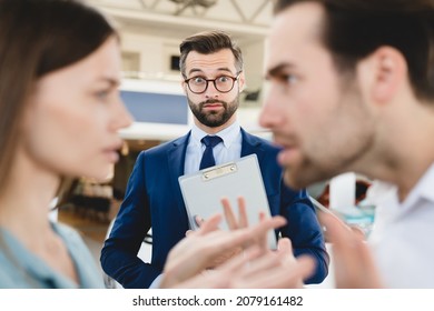 Confused Male Shop Assistant Looking At Angry Arguing Young Family Caucasian Couple While They Are Deciding Which Car Auto To Choose Buy. Expensive High Price.