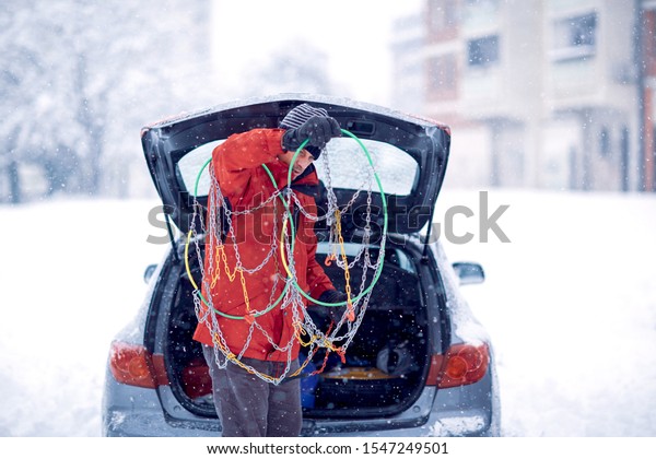 Confused man does not know how to put snow chains on\
car tire.Confused man with gloves install snow chains in the car\
tyre in winter on snow