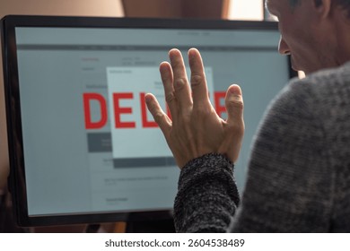Confused man looking at computer screen with text delete and having debt problems. Man focused on computer monitor, preparing to delete account and erase data