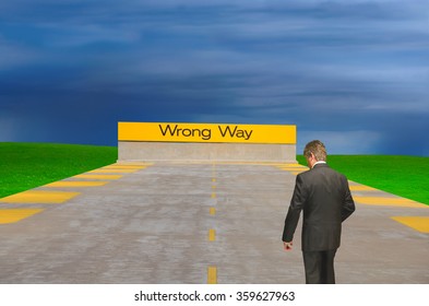 A Confused Man Looking Down Is Walking Towards A Sign That Says Wrong Way With A Stormy Ominous Sky In The Background.