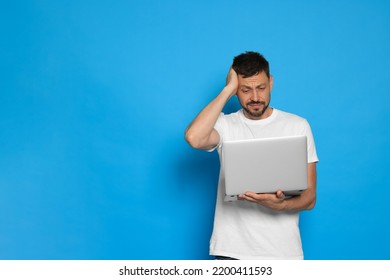 Confused Man Looking At Laptop On Light Blue Background. Space For Text