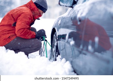 Confused man putting snow chains on car tire