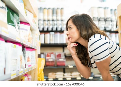 Confused mid adult woman choosing food products on shelf in grocery store