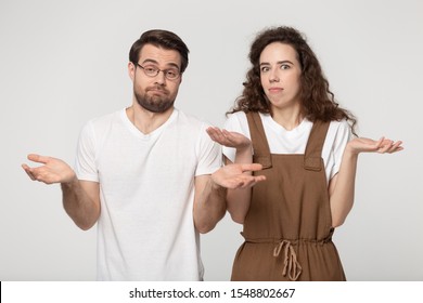 Confused Millennial Couple Isolated On Grey Studio Background Shrug Shoulders Feel At Lose Question Issue, Unsure Doubtful Man And Woman Lift Hands Baffled Hesitant About Problem, Having Dilemma