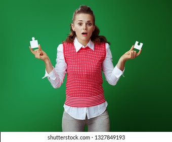 Confused Modern Learner Woman In Grey Jeans And Pink Sleeveless Shirt With A 2 Pieces Of The Puzzle Isolated On Green. Lack Of Analytical Thinking, Real-world Issues And Problems Solving