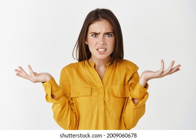 Confused and nervous woman asking what, spread hands sideways and staring at camera puzzled, cant understand whats happening, standing over white background