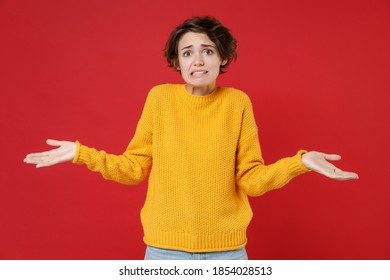 Confused puzzled concerned worried young brunette woman 20s wearing basic casual yellow sweater standing spreading hands looking camera isolated on bright red colour wall background studio portrait - Powered by Shutterstock