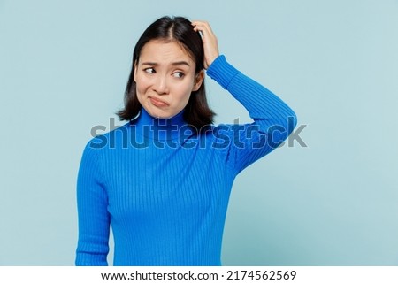 Confused puzzled preoccupied young woman of Asian ethnicity 20s years old wears blue shirt look aside think put hand on head have no idea isolated on plain pastel light blue background studio portrait