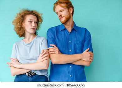 Confused Redhead Couple Looking At Each Other While Posing With Arms Crossed Isolated Over Blue Background