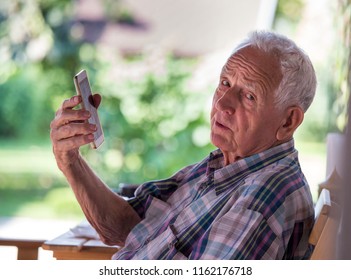 Confused Senior Man Sitting In Park And Talking On Cell Phone