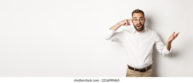 Confused And Shocked Man Pointing At Head, Scolding Employee For Acting Stupid, Standing Over White Background.