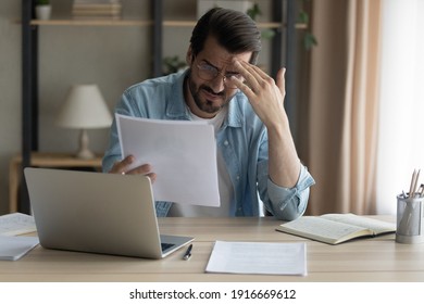 Confused shocked self employed businessman holding paper letter informing about accumulated bank debt unexpected financial problem. Upset stressed young male enterpreneur get loan application rejected - Shutterstock ID 1916669612