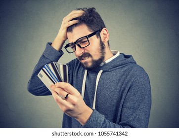 Confused stressed man looking at too many credit cards full of debt  - Shutterstock ID 1055741342