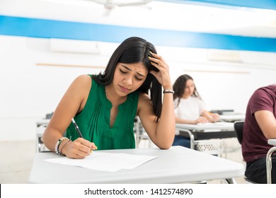 Confused Student Writing Exam In Classroom At College