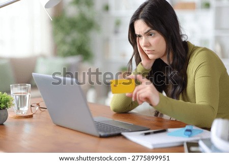 Confused and suspicious student having problems paying online with credit card and laptop at home