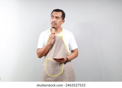 Confused thougthful man barista barman employee wear brown apron work in coffee shop write down order in notebook isolated on gray background. Small business startup concept - Powered by Shutterstock