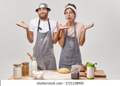 Confused Unaware Young Woman And Man Spread Hands Sideways, Stand Puzzled, Prepare Cookies, Make Dough, Dont Know Which Product To Choose. Questioned Family Couple Pose Together At Kitchen Room