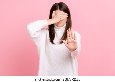 Confused Woman Covers Eyes, Raising Hand To Stop, Feeling Stressed, Refusing To Watch Scary Content, Wearing White Casual Style Sweater. Indoor Studio Shot Isolated On Pink Background.