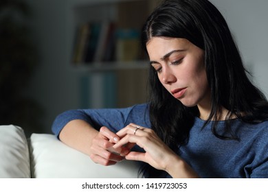 Confused Woman Looking At Engagement Ring Sitting On A Couch In The Night At Home