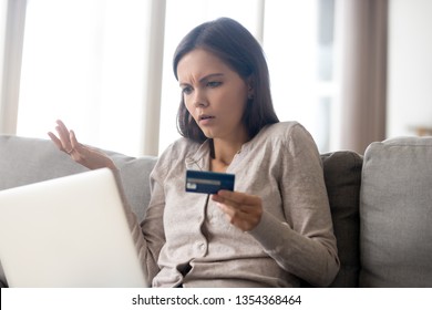 Confused woman sitting on couch holds credit card use laptop looking at device screen having debt problems, transaction failed, money withdraw impossible, insecure online payment or scam fraud concept