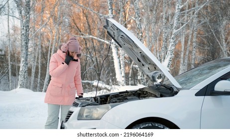 Confused Woman Talking On Phone, Calling For Help While Standing By The Open Hood Of Her Broken Car In Cold Winter Day