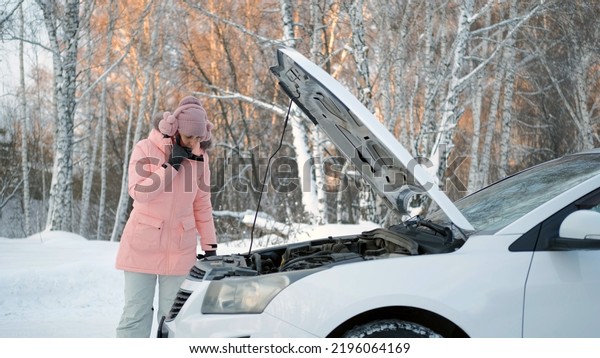 Confused Woman\
Talking on Phone, Calling for Help while Standing by the Open Hood\
of her Broken Car in Cold Winter\
Day