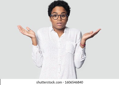 Confused young african ethnicity woman in glasses being in perplexity shrugged her shoulders raised palms gawp at camera looking puzzled posing isolated on gray studio background, I dont know concept